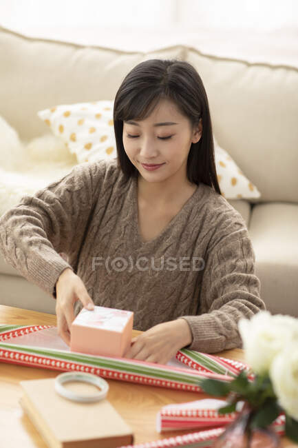 Joven mujer china envolviendo regalo en la sala de estar - foto de stock