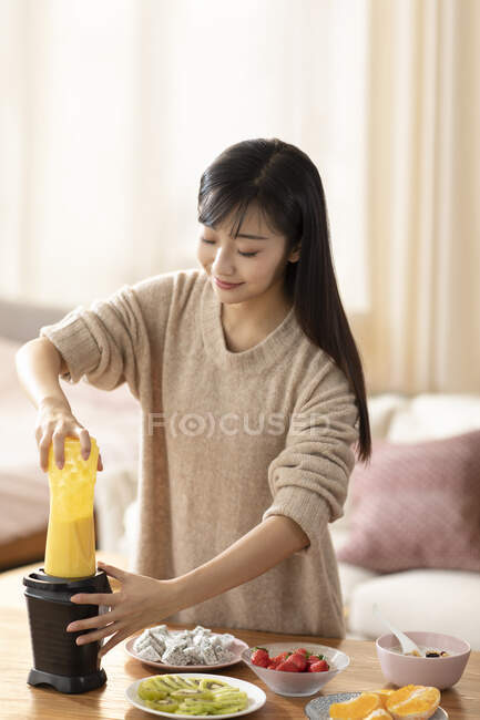 Joven mujer china haciendo jugo en casa - foto de stock