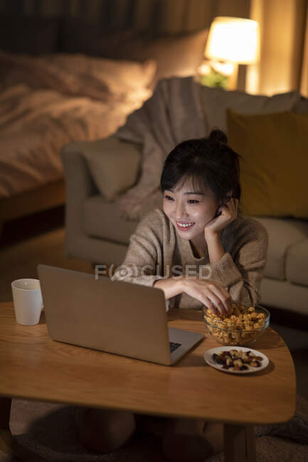 Жінка дивиться фільм на ноутбуці і приймає закуски з миски — стокове фото