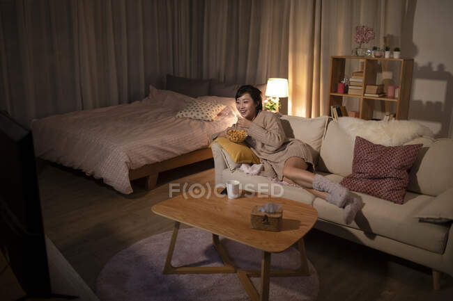 Giovane donna cinese guardando la TV sul divano — Foto stock