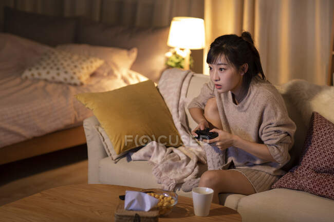 Joven mujer china jugando videojuego en el sofá - foto de stock