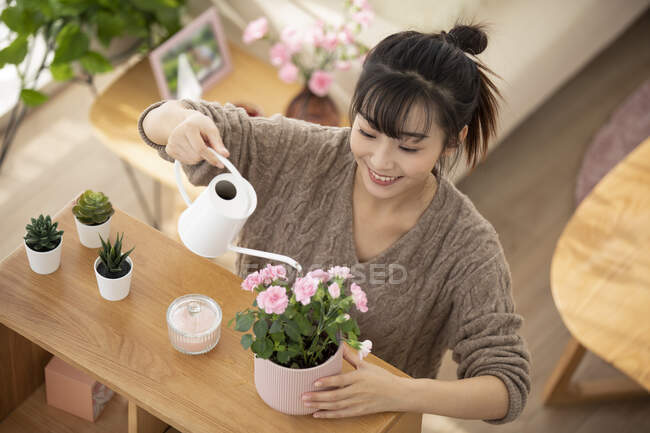 Молода китайка поливає квіти вдома. — стокове фото