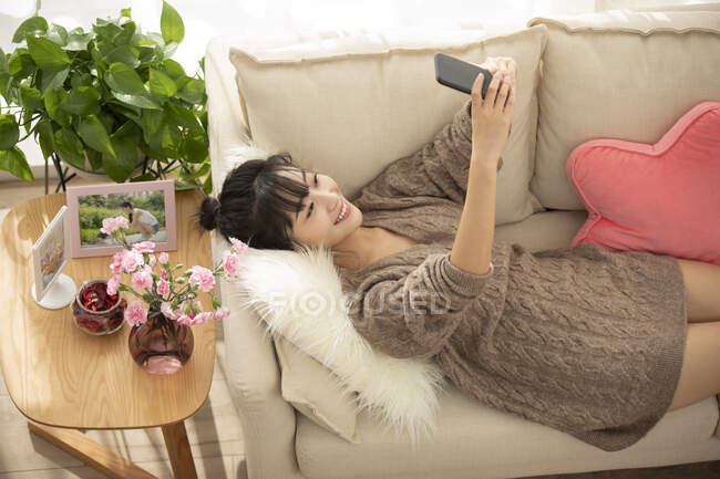 Jovem chinesa usando smartphone no sofá — Fotografia de Stock
