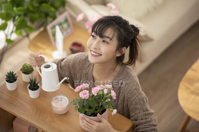 Young Chinese woman watering flowers at home — Stock Photo