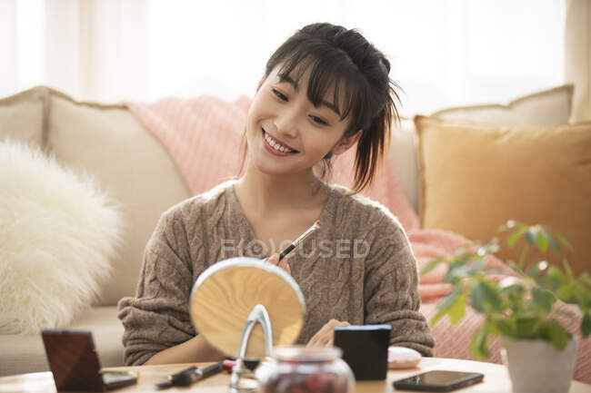 Mujer aplicando maquillaje en una pequeña mesa por sofá - foto de stock