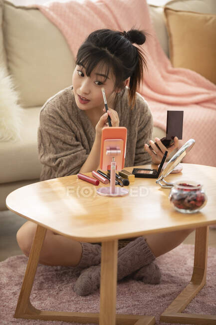 Woman applying makeup on small table by couch — Stock Photo