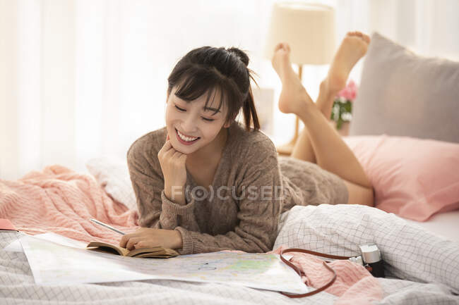 Femme faisant un plan de voyage à la maison, couchée sur le lit avec carte — Photo de stock