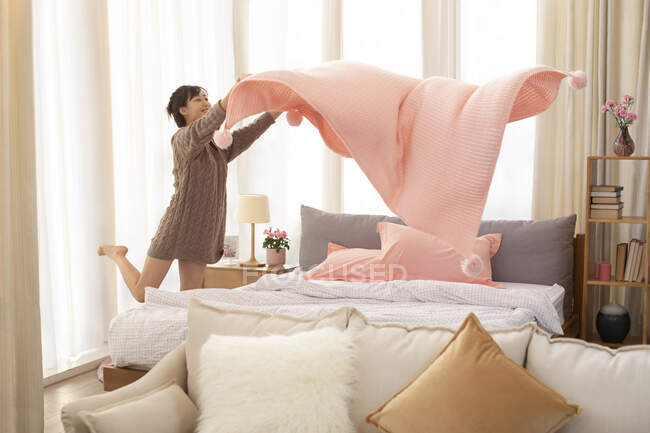 Молодая китаянка застилает постель дома — стоковое фото