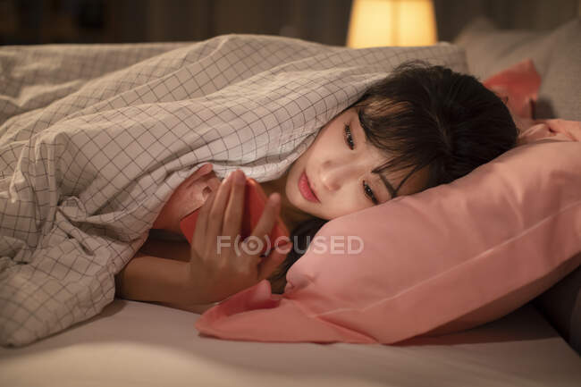 Giovane donna cinese utilizzando smartphone a letto — Foto stock