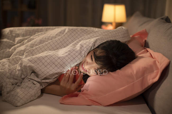 Giovane donna cinese utilizzando smartphone a letto — Foto stock
