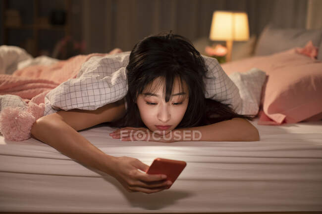 Jovem mulher chinesa usando smartphone na cama — Fotografia de Stock