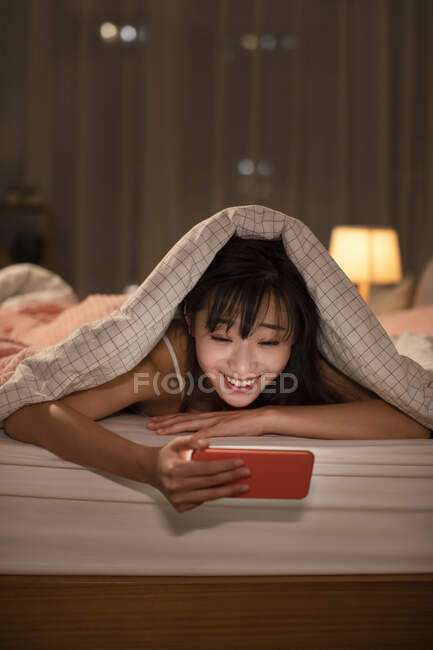 Mujer china joven usando teléfono inteligente en la cama - foto de stock