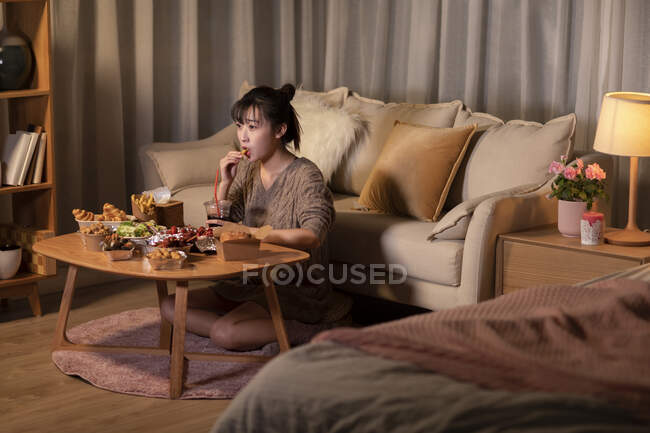Mujer comiendo sacar comida en la sala de estar por la noche - foto de stock