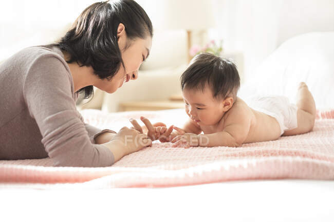 Junge chinesische Mutter lächelt und spielt mit Baby auf Couch — Stockfoto