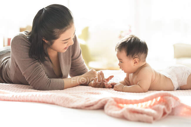 Молодая китайская мама улыбается и играет с ребенком на диване — стоковое фото