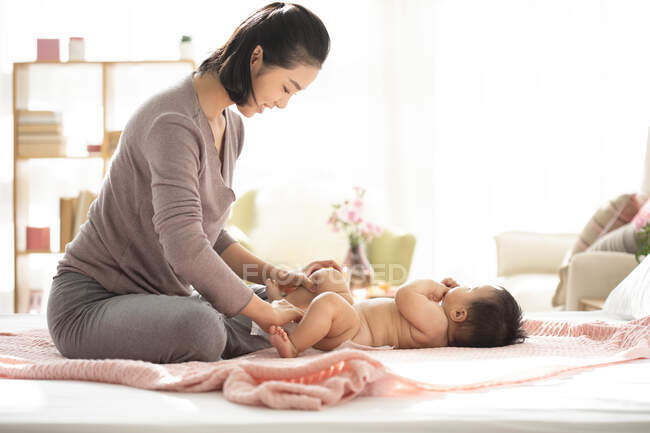 Young chinese mom changing baby's diaper — Stock Photo