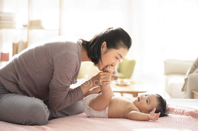 Young chinese mom kissing baby's feet — Stock Photo