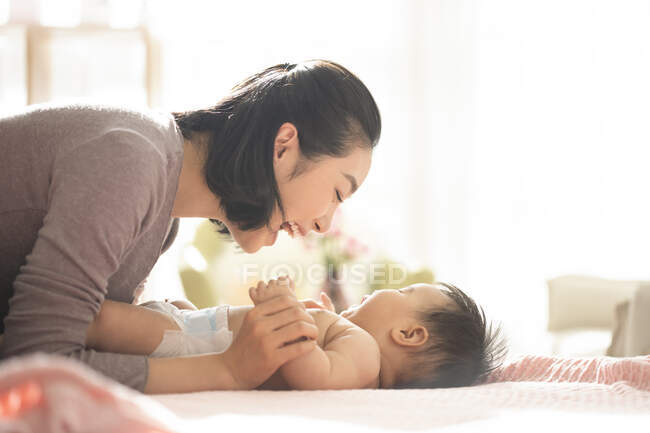 Jeune maman chinoise souriant et jouant avec bébé sur le canapé — Photo de stock
