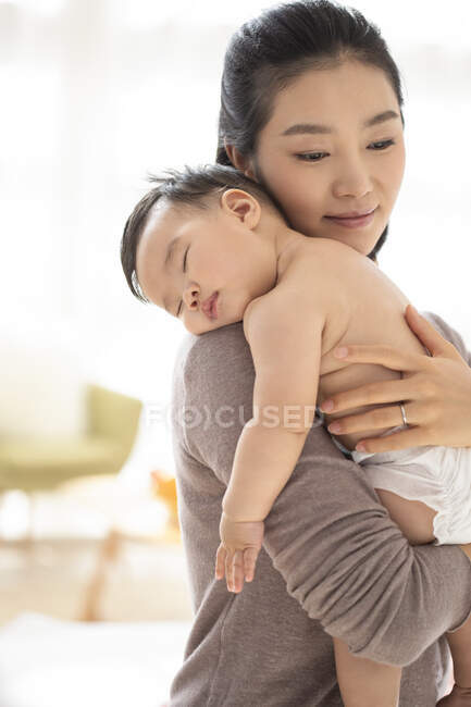 Joven madre china sosteniendo a su bebé dormido - foto de stock
