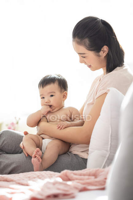 Молодая китайская мама держит своего ребенка, сидя на диване — стоковое фото