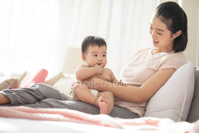Jeune maman chinoise tenant son bébé tout en étant assis sur le canapé — Photo de stock