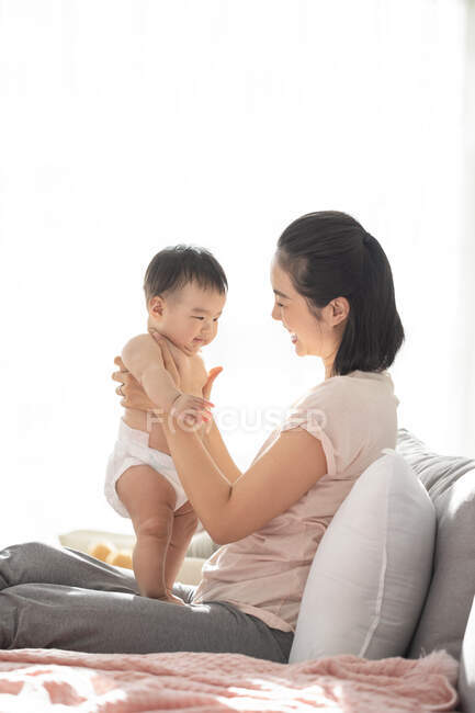 Молодая китайская мама держит своего ребенка, сидя на диване — стоковое фото