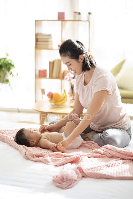 Молода китайська мама посміхається і грає з дитиною на дивані — стокове фото