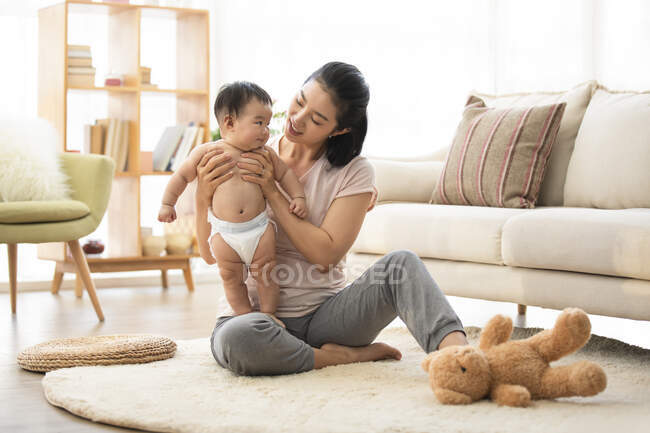 Mamá sosteniendo al bebé en el suelo en la sala de estar - foto de stock