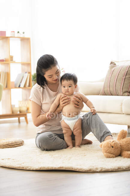 Mãe segurando bebê no chão na sala de estar — Fotografia de Stock