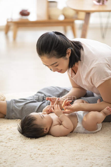 Jeune mère jouer avec bébé couché sur le tapis — Photo de stock