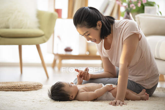 Junge Mutter spielt mit Baby auf Teppich liegend — Stockfoto