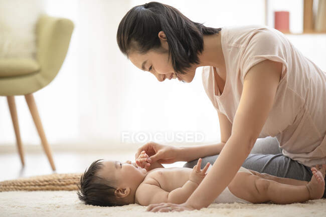 Jovem mãe brincando com bebê deitado no tapete — Fotografia de Stock