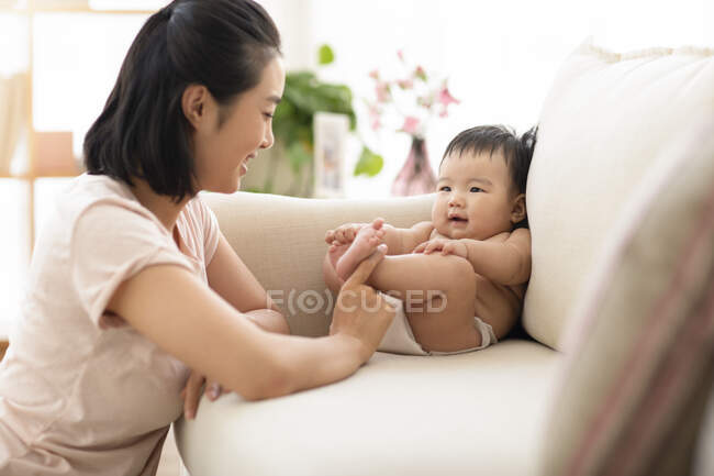 Jovem mãe brincando com o bebê no sofá — Fotografia de Stock