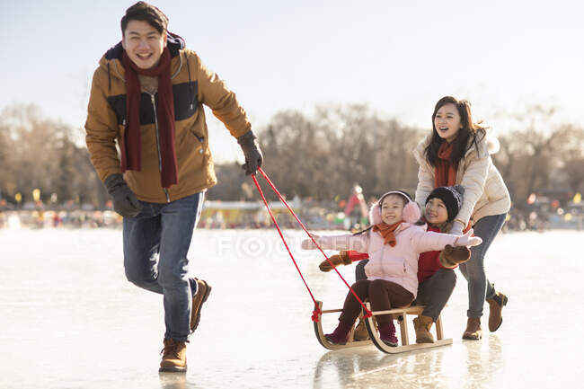 Happy young Chinese family sledding outdoors — Stock Photo