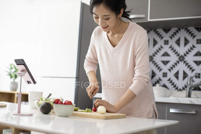 Young Chinese woman chopping tomato on wooden board for salad — Stock Photo