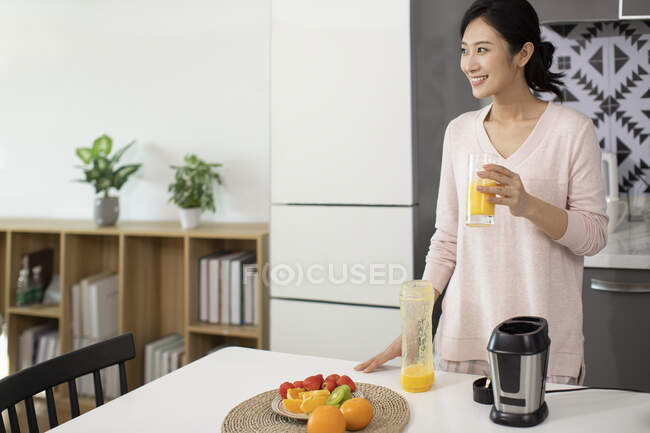 Heureuse jeune femme chinoise tenant un verre de jus frais et détournant les yeux — Photo de stock