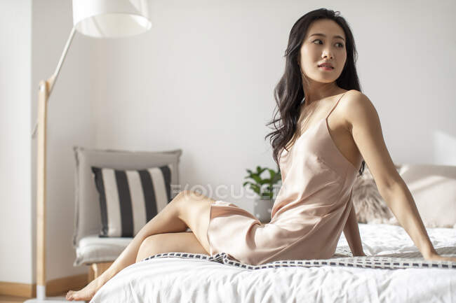 Junge Chinesin sitzt im Nachthemd auf dem Bett — Stockfoto