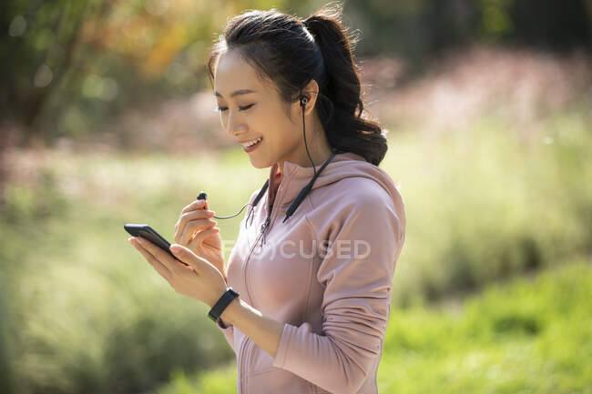 Mulher em roupas esportivas usando smartphone e fones de ouvido — Fotografia de Stock