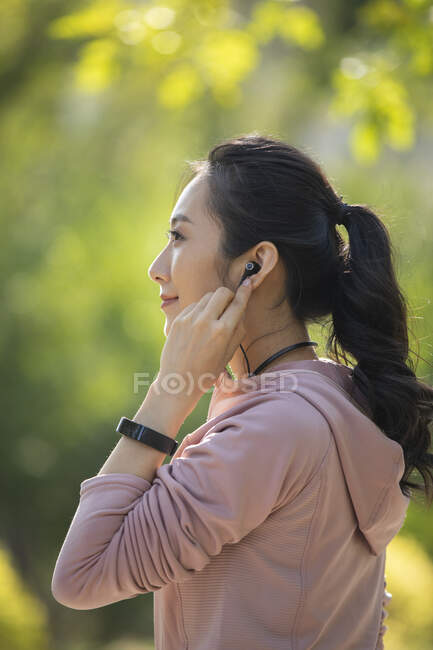 Mujer con pulsera de fitness a mano poniendo auriculares en - foto de stock
