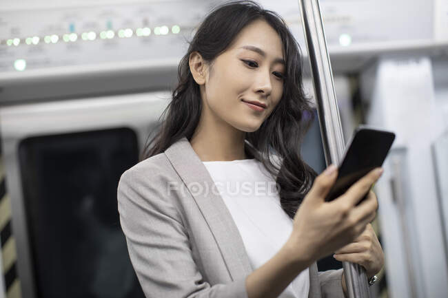 Jeune femme d'affaires chinoise utilisant un smartphone dans le métro — Photo de stock