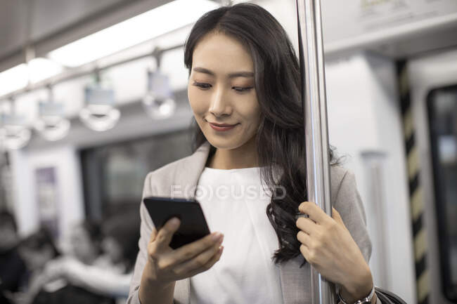 Молода китайська комерсантка користується смартфоном у метро. — стокове фото