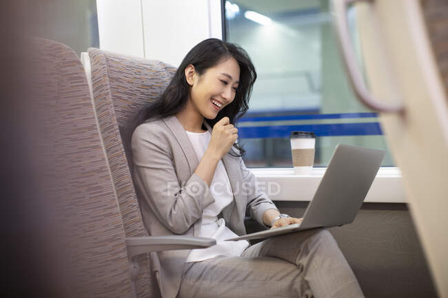 Smiling woman sitting in high-speed train with coffee cup and using laptop — Stock Photo