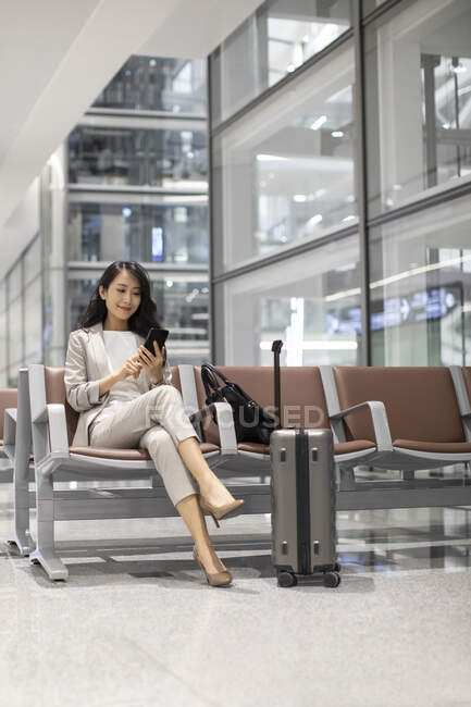 Mujer usando teléfono inteligente mientras está sentado en el aeropuerto - foto de stock