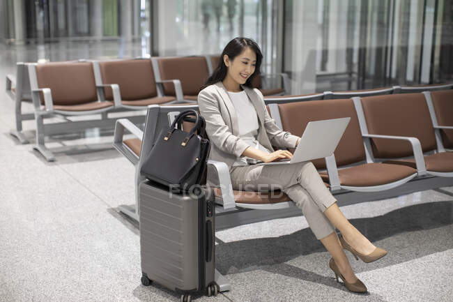 Жінка використовує ноутбук, сидячи в аеропорту — стокове фото
