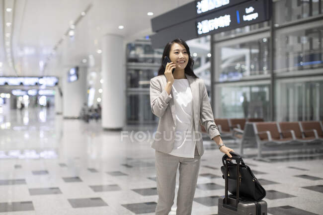 Woman with luggage talking on phone in airport — Stock Photo