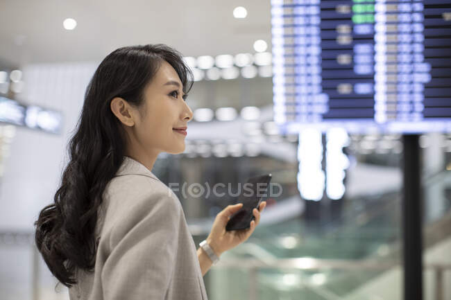 Jovem chinesa usando smartphone no aeroporto — Fotografia de Stock