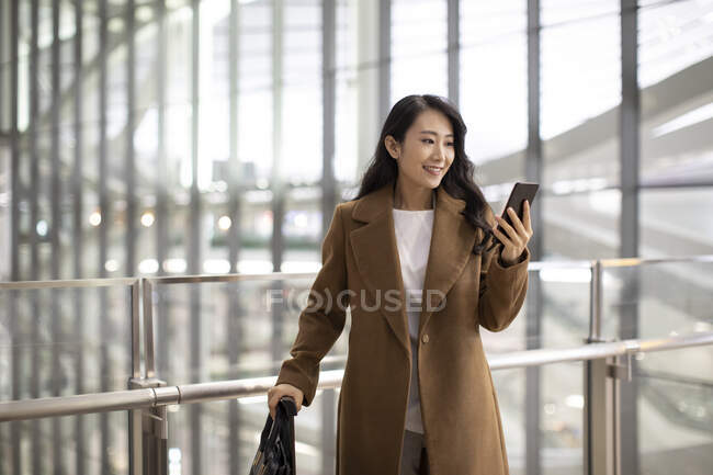 Жінка зі смартфоном і багажем в аеропорту — стокове фото