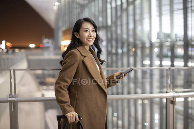 Женщина со смартфоном и багажом в аэропорту — стоковое фото