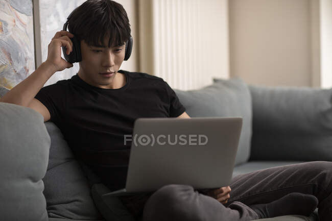 Молодий китайський чоловік в навушниках дивиться на екран ноутбука — стокове фото