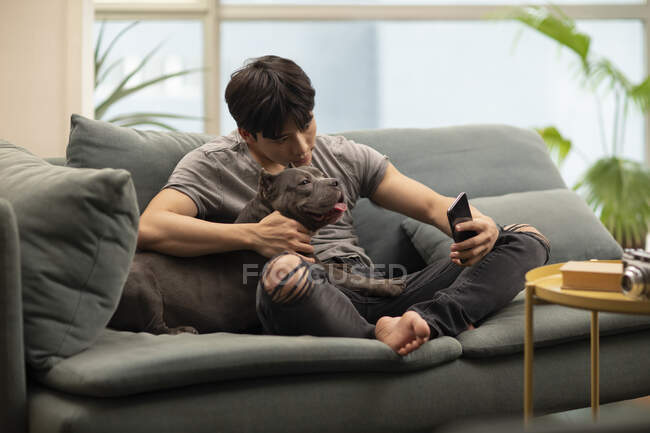 Giovane cinese che prende selfie con cane sul divano — Foto stock